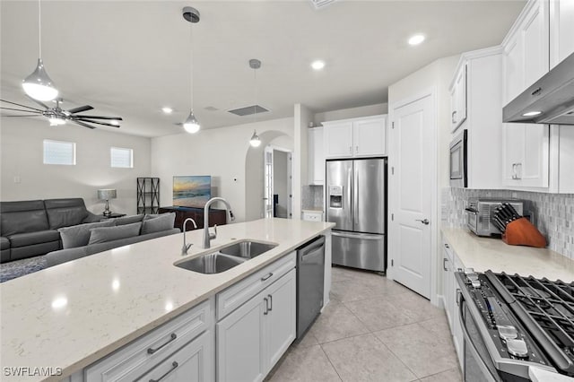 kitchen with wall chimney exhaust hood, stainless steel appliances, white cabinetry, a sink, and light tile patterned floors