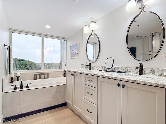 bathroom with hardwood / wood-style flooring, vanity, and tiled bath