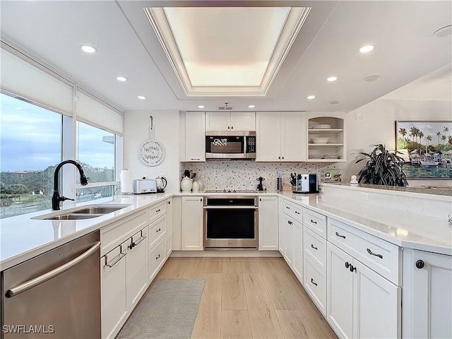 kitchen with a raised ceiling, sink, white cabinets, stainless steel appliances, and light wood-type flooring