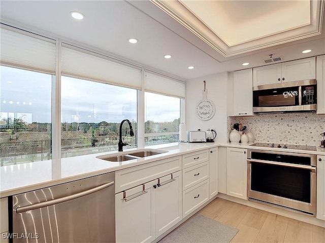 kitchen featuring sink, appliances with stainless steel finishes, white cabinetry, tasteful backsplash, and light hardwood / wood-style floors