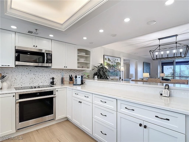 kitchen with tasteful backsplash, hanging light fixtures, light wood-type flooring, appliances with stainless steel finishes, and white cabinets