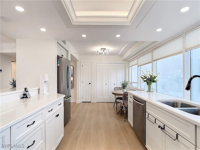 kitchen with sink, light wood-type flooring, a raised ceiling, stainless steel appliances, and white cabinets