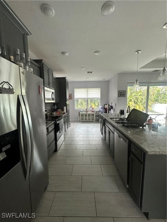 kitchen with a wealth of natural light, appliances with stainless steel finishes, pendant lighting, and dark stone counters