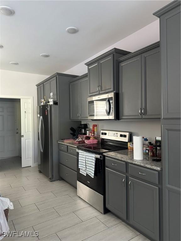 kitchen with appliances with stainless steel finishes, gray cabinets, and dark stone countertops