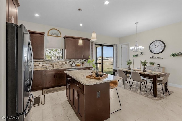 kitchen with light stone countertops, a kitchen island, sink, hanging light fixtures, and stainless steel refrigerator