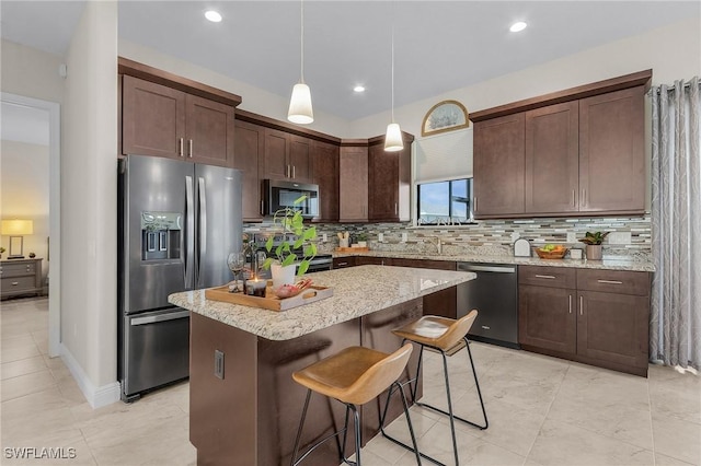 kitchen with appliances with stainless steel finishes, decorative backsplash, decorative light fixtures, dark brown cabinets, and a kitchen island