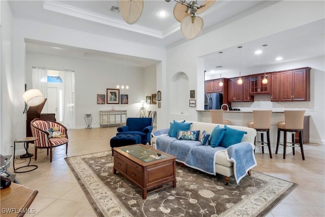 tiled living room with a raised ceiling, a high ceiling, ceiling fan, and crown molding