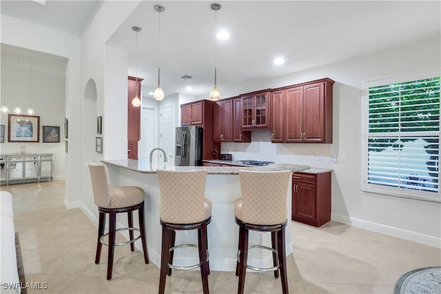 kitchen featuring backsplash, kitchen peninsula, hanging light fixtures, a breakfast bar area, and stainless steel fridge