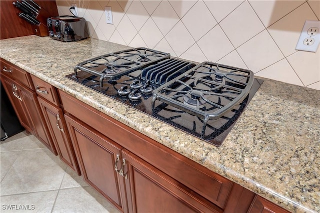 interior details featuring decorative backsplash, light stone countertops, and black gas cooktop