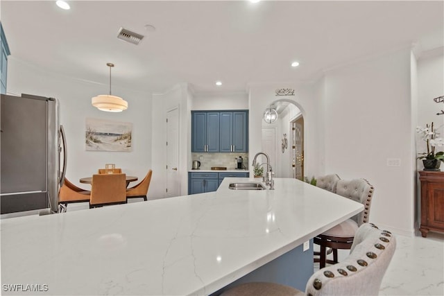 kitchen with decorative light fixtures, sink, stainless steel refrigerator, ornamental molding, and blue cabinets