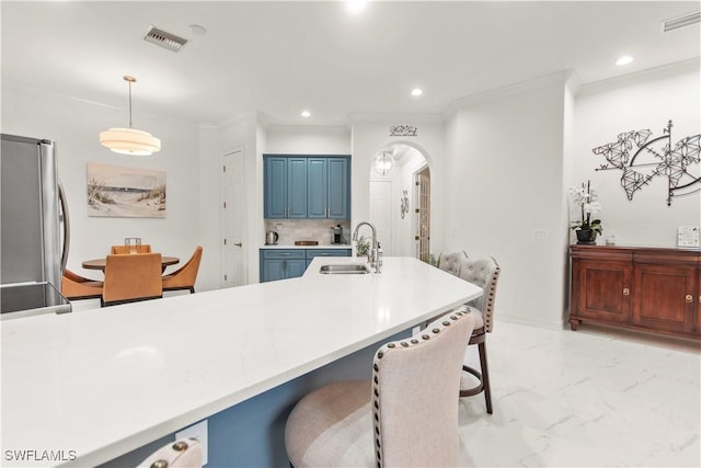 kitchen featuring sink, stainless steel refrigerator, crown molding, hanging light fixtures, and a kitchen breakfast bar