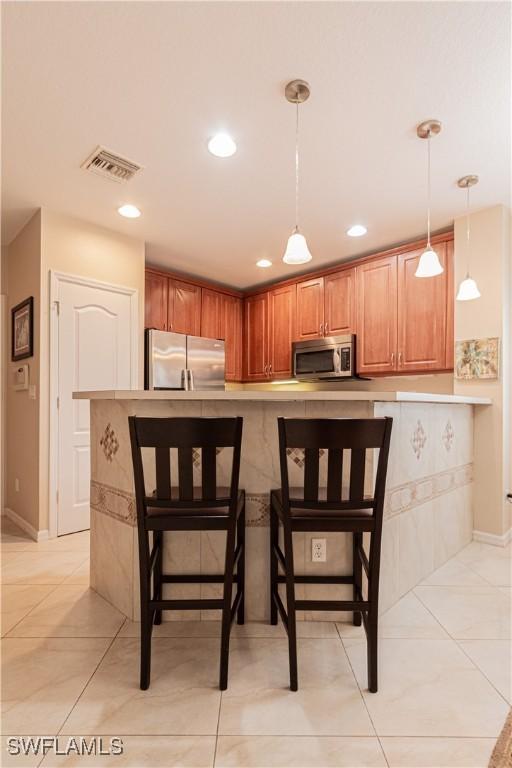 kitchen with a kitchen bar, hanging light fixtures, stainless steel appliances, and light tile patterned flooring