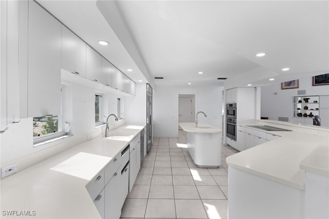 kitchen with white cabinets, sink, light tile patterned floors, and a center island with sink