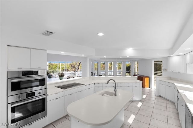 kitchen featuring black electric stovetop, double oven, a center island with sink, and sink