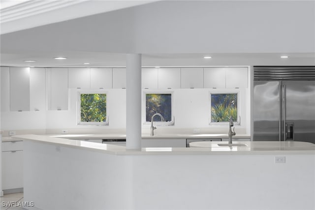 kitchen with white cabinets, sink, built in fridge, and dishwashing machine