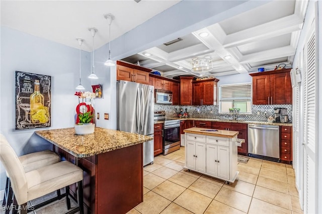 kitchen with coffered ceiling, a center island, hanging light fixtures, beamed ceiling, and stainless steel appliances