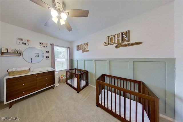 carpeted bedroom with ceiling fan and a nursery area