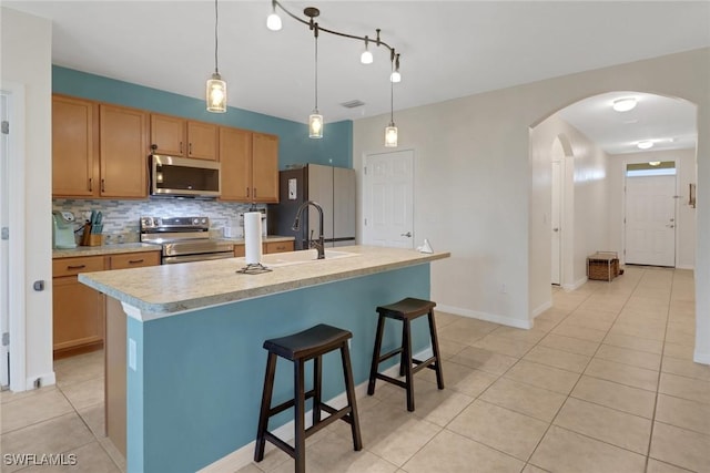 kitchen with a kitchen island with sink, backsplash, stainless steel appliances, and pendant lighting