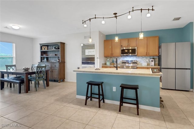 kitchen featuring stainless steel appliances, tasteful backsplash, a breakfast bar, and a kitchen island with sink