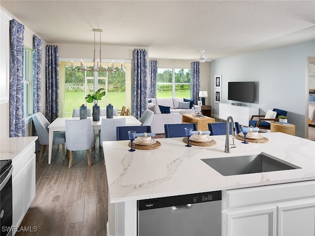 kitchen with pendant lighting, sink, a kitchen island with sink, light stone counters, and stainless steel dishwasher