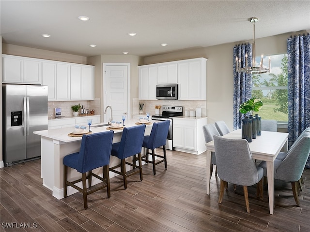 kitchen featuring white cabinets, a center island with sink, appliances with stainless steel finishes, and pendant lighting