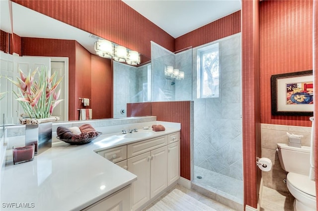 bathroom with toilet, tiled shower, tile walls, tile patterned floors, and vanity