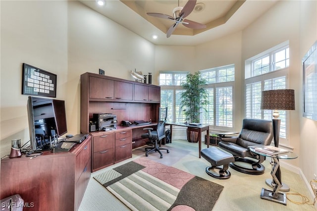 office featuring ceiling fan, light colored carpet, a high ceiling, and a tray ceiling