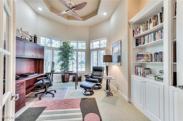 carpeted office featuring ceiling fan, a towering ceiling, a tray ceiling, and built in shelves