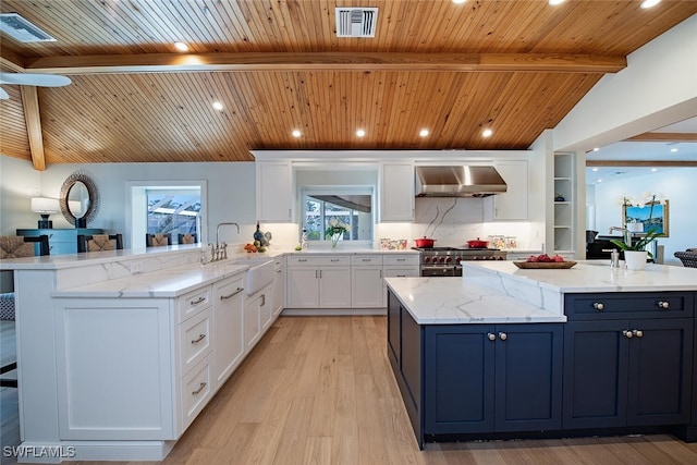 kitchen featuring wall chimney range hood, a sink, white cabinets, wooden ceiling, and light stone countertops