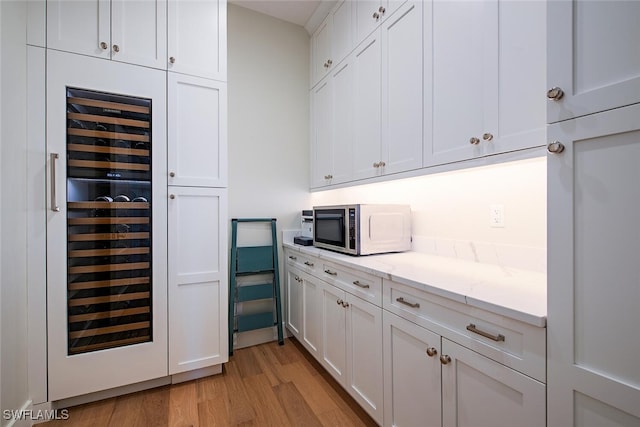 bar with wine cooler, light stone countertops, light hardwood / wood-style flooring, and white cabinets