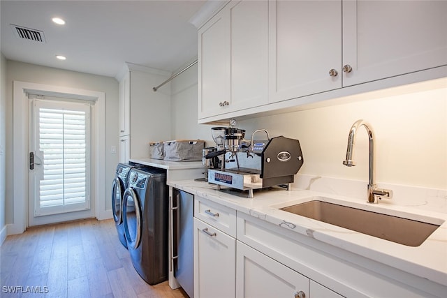 clothes washing area with cabinets, sink, washer and clothes dryer, and light hardwood / wood-style floors