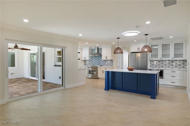 kitchen featuring decorative light fixtures, a kitchen island, white cabinetry, appliances with stainless steel finishes, and wall chimney exhaust hood