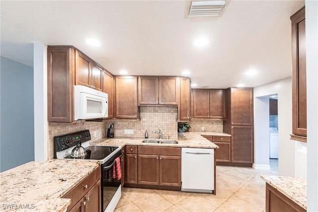 kitchen featuring white appliances, washer / clothes dryer, light stone countertops, and sink