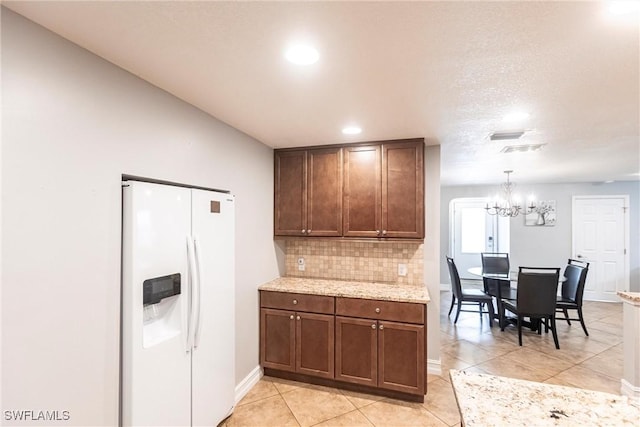 kitchen featuring backsplash, a chandelier, hanging light fixtures, white refrigerator with ice dispenser, and light tile patterned floors