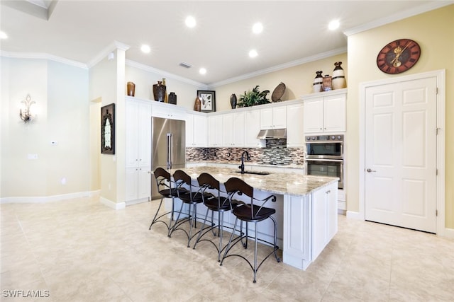 kitchen with a breakfast bar area, light stone counters, crown molding, a center island with sink, and white cabinets