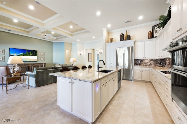 kitchen featuring sink, stainless steel appliances, coffered ceiling, an island with sink, and white cabinets