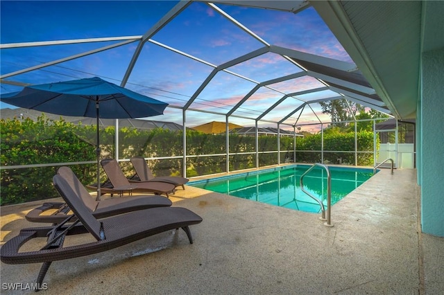 pool at dusk with glass enclosure and a patio area