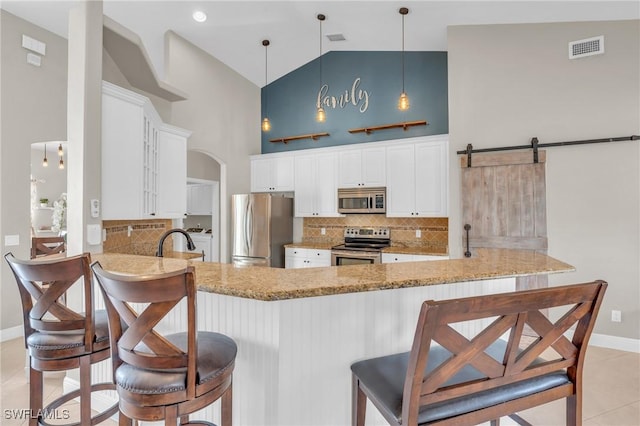 kitchen featuring a barn door, pendant lighting, kitchen peninsula, appliances with stainless steel finishes, and high vaulted ceiling