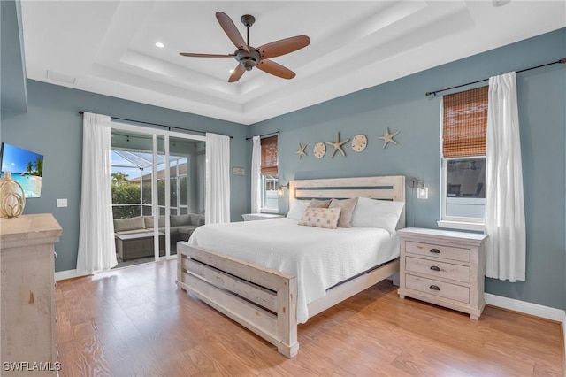 bedroom featuring ceiling fan, access to exterior, a tray ceiling, and light hardwood / wood-style flooring