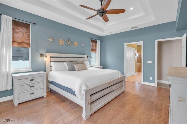 bedroom with light wood-type flooring, ceiling fan, and a tray ceiling