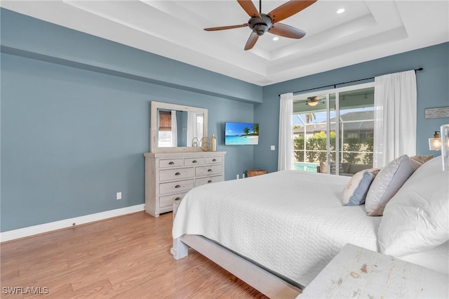 bedroom with ceiling fan, a tray ceiling, and light hardwood / wood-style flooring