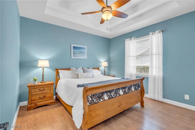 bedroom featuring ceiling fan, light hardwood / wood-style flooring, and a raised ceiling