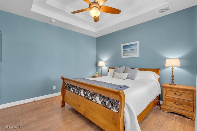 bedroom featuring ceiling fan, a tray ceiling, and light hardwood / wood-style floors