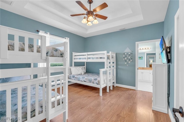 bedroom with a raised ceiling, ceiling fan, ensuite bathroom, and light hardwood / wood-style floors