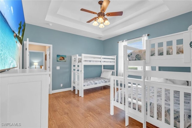 bedroom featuring ceiling fan, light wood-type flooring, and a tray ceiling