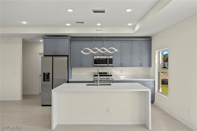 kitchen with stainless steel appliances, gray cabinetry, a center island with sink, and sink