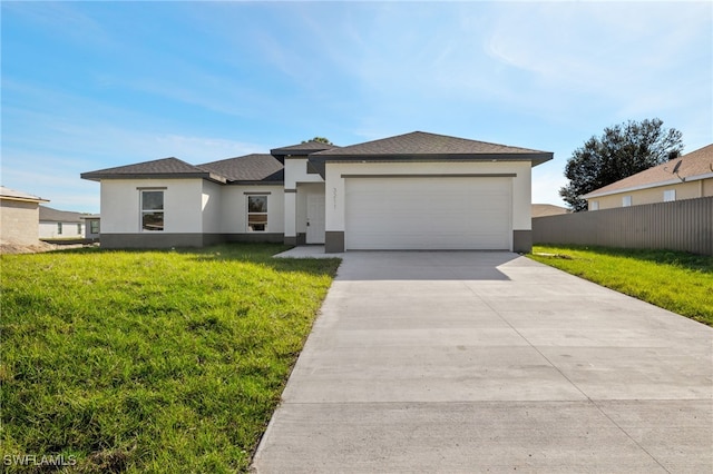 prairie-style house featuring driveway, fence, a garage, a front yard, and stucco siding