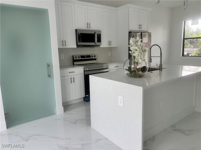 3204 20th St SW, Lehigh Acres, FL 33976 - kitchen featuring appliances with stainless steel finishes, light marble finish flooring, white cabinets, a center island with sink, and light stone counters