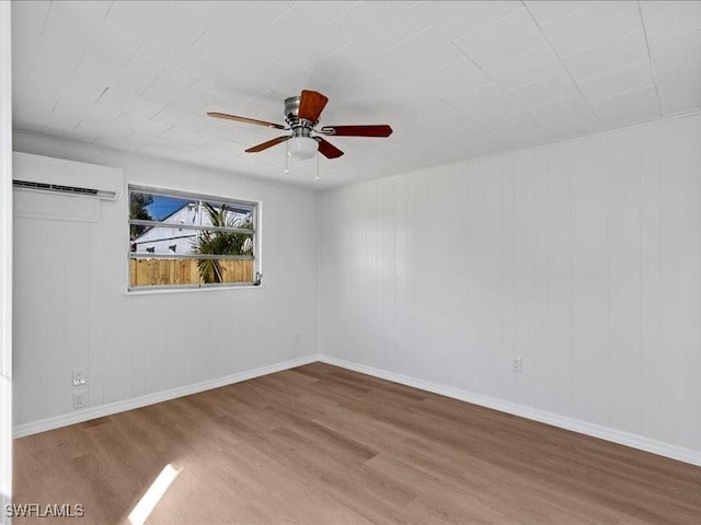 empty room featuring ceiling fan, hardwood / wood-style floors, a barn door, and a wall unit AC