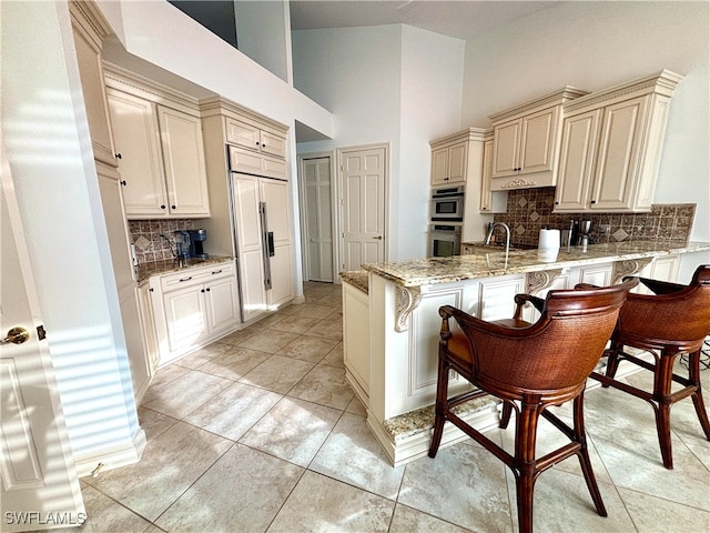 kitchen with a peninsula, cream cabinetry, a breakfast bar, and light stone countertops